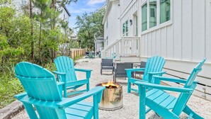 A patio area with turquoise Adirondack chairs arranged around a fire pit, a dining table, and a white building in the background. - "Shore To Please" - Cottages at Seagrove - 5 Bed / 5.5 Bath - Sleeps 14 - Across from the Pool! (Santa Rosa Beach)