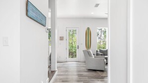 A hallway with a wooden floor, a door with glass panels, and a surfboard mounted on the wall. - "Shore To Please" - Cottages at Seagrove - 5 Bed / 5.5 Bath - Sleeps 14 - Across from the Pool! (Santa Rosa Beach)