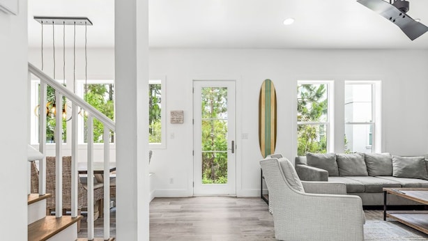 A spacious living area with a staircase, a sofa, and a surfboard against the wall. - "Shore To Please" - Cottages at Seagrove - 5 Bed / 5.5 Bath - Sleeps 14 - Across from the Pool! (Santa Rosa Beach)