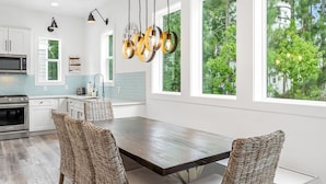 A modern kitchen with white cabinets, a stainless steel microwave, and a wooden dining table with woven chairs. - "Shore To Please" - Cottages at Seagrove - 5 Bed / 5.5 Bath - Sleeps 14 - Across from the Pool! (Santa Rosa Beach)