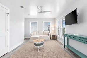 A modern living room with a sofa, a coffee table, a TV, and a ceiling fan.