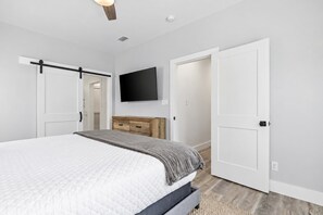 Une chambre à coucher avec un lit, une commode, un téléviseur à écran plat et une porte.