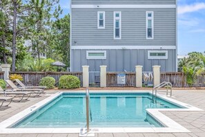 A swimming pool with a wooden deck, lounge chairs, and a building with a grey facade in the background.