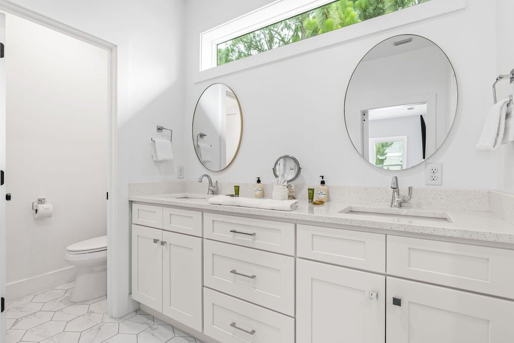 A modern bathroom with a white sink, two mirrors, and a toilet.
