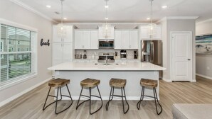 A modern kitchen with white cabinets, stainless steel appliances, and a central island with stools. - Beautiful Villa in Lost Key | EV Charger | Screened Balcony | Private Beach Club | Pools | Free Golf (Pensacola)