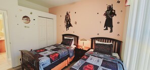 Quarto com roupa de cama temática de Star Wars, duas camas, uma mesinha de cabeceira e adesivos de parede de Star Wars.