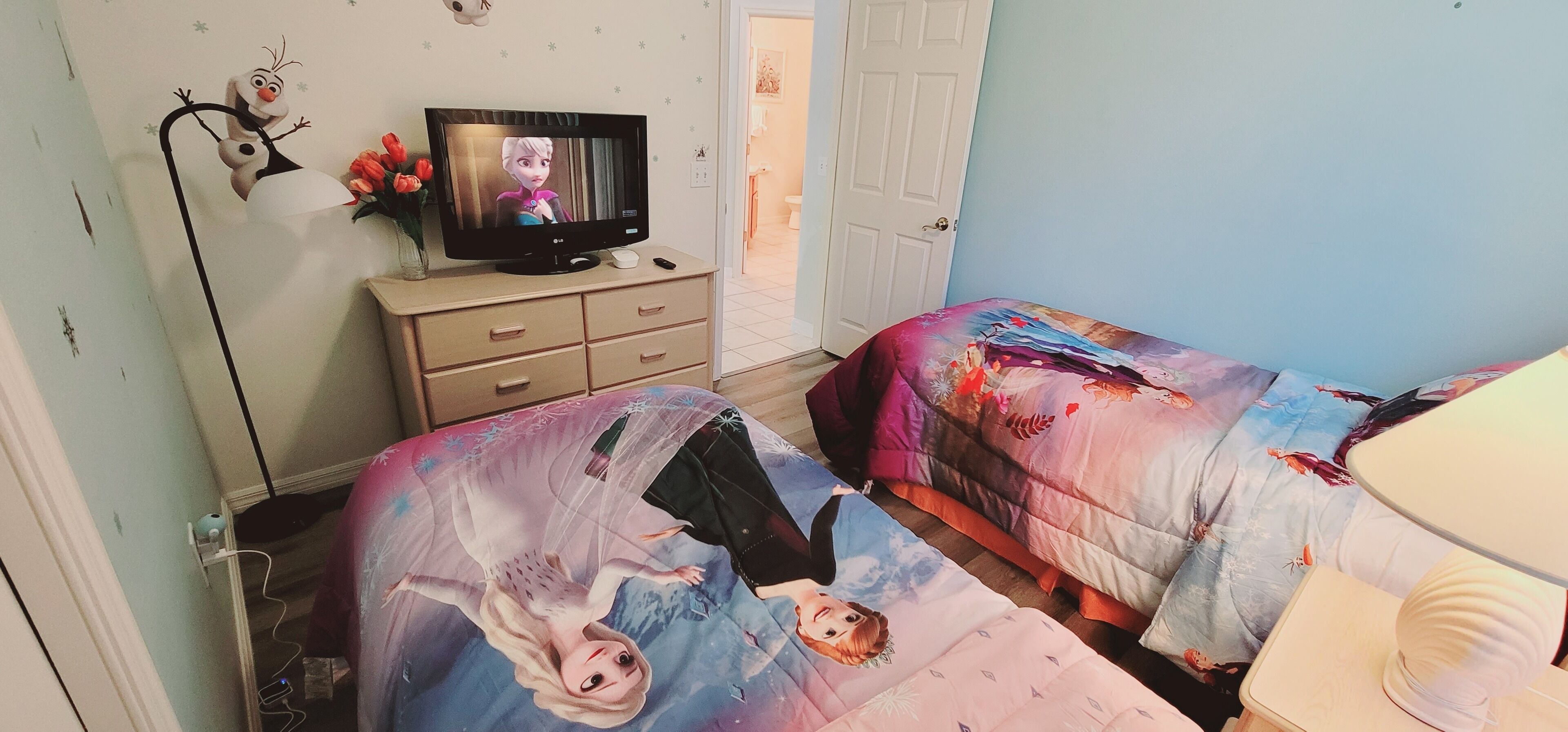 A bedroom with two beds, a TV on a dresser, and a door leading to another room.
