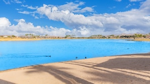Une vaste étendue d’eau calme, bordée d’une plage de sable, et un ciel bleu clair parsemé de quelques nuages.
