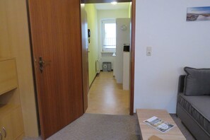 A hallway leading to a room with a window, a door, a small table, and a sofa.