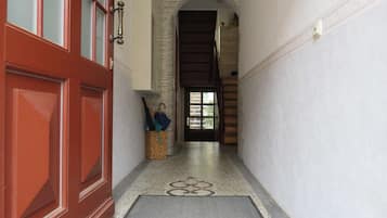 Un pasillo con una puerta roja, un banco de madera, una cesta y una escalera que sube a un nivel superior.