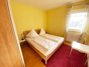 Une chambre avec deux lits, un bureau, un radiateur et une fenêtre avec des rideaux.
