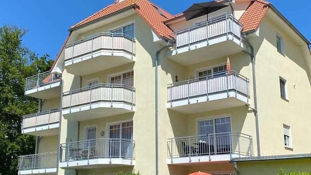 A multi-story residential building with balconies, a red-tiled roof, and a well-maintained garden area. - Vacation apartment 25 Nachtigallenweg (Graal-Müritz)
