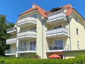 A multi-story residential building with balconies, a red-tiled roof, and a well-maintained garden area. - Vacation apartment 25 Nachtigallenweg (Graal-Müritz)