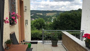 Un balcone con vista su un paesaggio verde, un tavolo con sedie e piante in vaso.
