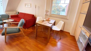 A modern living room with a red sofa, a dining table, and a kitchen area with a refrigerator. - Vacation apartment Haus Küste 9 (Graal-Müritz)
