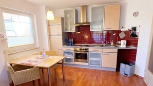 A compact kitchen with a dining area, featuring a table with chairs, a built-in oven, a stove, and a sink. - Vacation apartment Haus Küste 9 (Graal-Müritz)