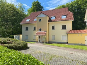 A two-story building with a red-tiled roof, a central entrance, and a small porch.
