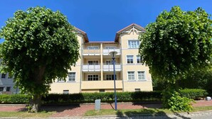 A multi-story residential building with balconies, a paved courtyard, and mature trees. - Vacation apartment Seeadler 1 (Graal-Müritz)