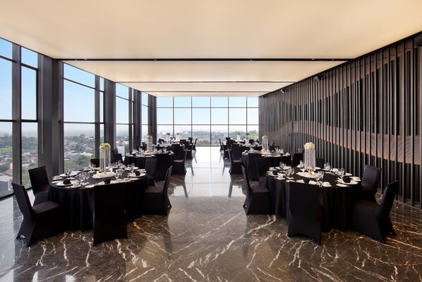 Un comedor amplio con techos altos y ventanas grandes que ofrecen vistas a la ciudad. Las mesas están dispuestas con porcelana fina y cristalería.