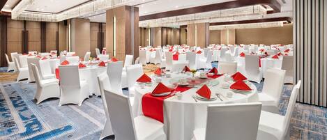A banquet hall with round tables, white chairs, and red napkins.