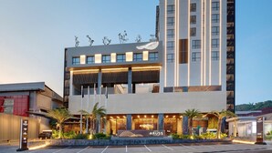 A modern hotel with a prominent entrance, a parking area, and a tall adjacent building. - Hotel Aruss Semarang (Semarang)