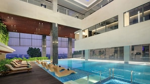 A modern indoor pool area with lounge chairs and a view of the cityscape. - Hotel Aruss Semarang (Semarang)