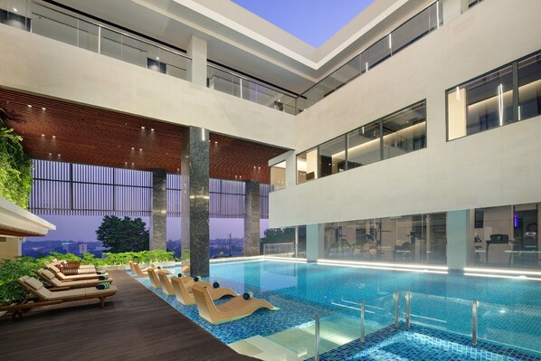 Un área de piscina interior moderna con sillones de descanso y vistas a la ciudad.