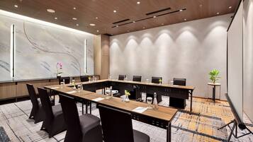 A conference room with a long table, black chairs, and a projector screen.