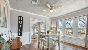 A hotel room with a wooden floor, a dining area with a table and chairs, a ceiling fan, and large windows. - Cute Cottage close in Downtown Waco close to Magnolia, Baylor Uni., Cameron Park (Waco)