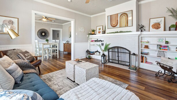 A living room with a fireplace, a ceiling fan, and a dining area with a table and chairs. - Cute Cottage close in Downtown Waco close to Magnolia, Baylor Uni., Cameron Park (Waco)