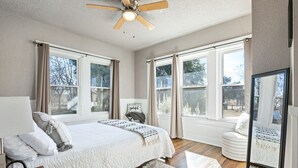 A spacious bedroom with a large bed, a ceiling fan, and multiple windows offering a view of the outdoors. - Cute Cottage close in Downtown Waco close to Magnolia, Baylor Uni., Cameron Park (Waco)