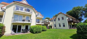 Ein mehrstöckiges Wohngebäude mit Balkonen, einer Terrasse mit Gartenmöbeln und einem gepflegten Rasen.