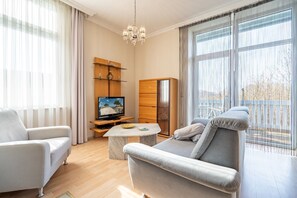 A modern living room with a sofa, armchair, TV, wooden shelves, and a chandelier. - Villa Seestern, apt. 3 (Heringsdorf)