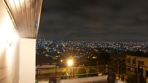 Ein Balkon mit Blick auf eine beleuchtete Stadtlandschaft bei Nacht.