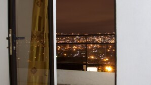 Ein Zimmer mit einer Schiebetür zu einem Balkon mit Blick auf die beleuchtete Stadt.