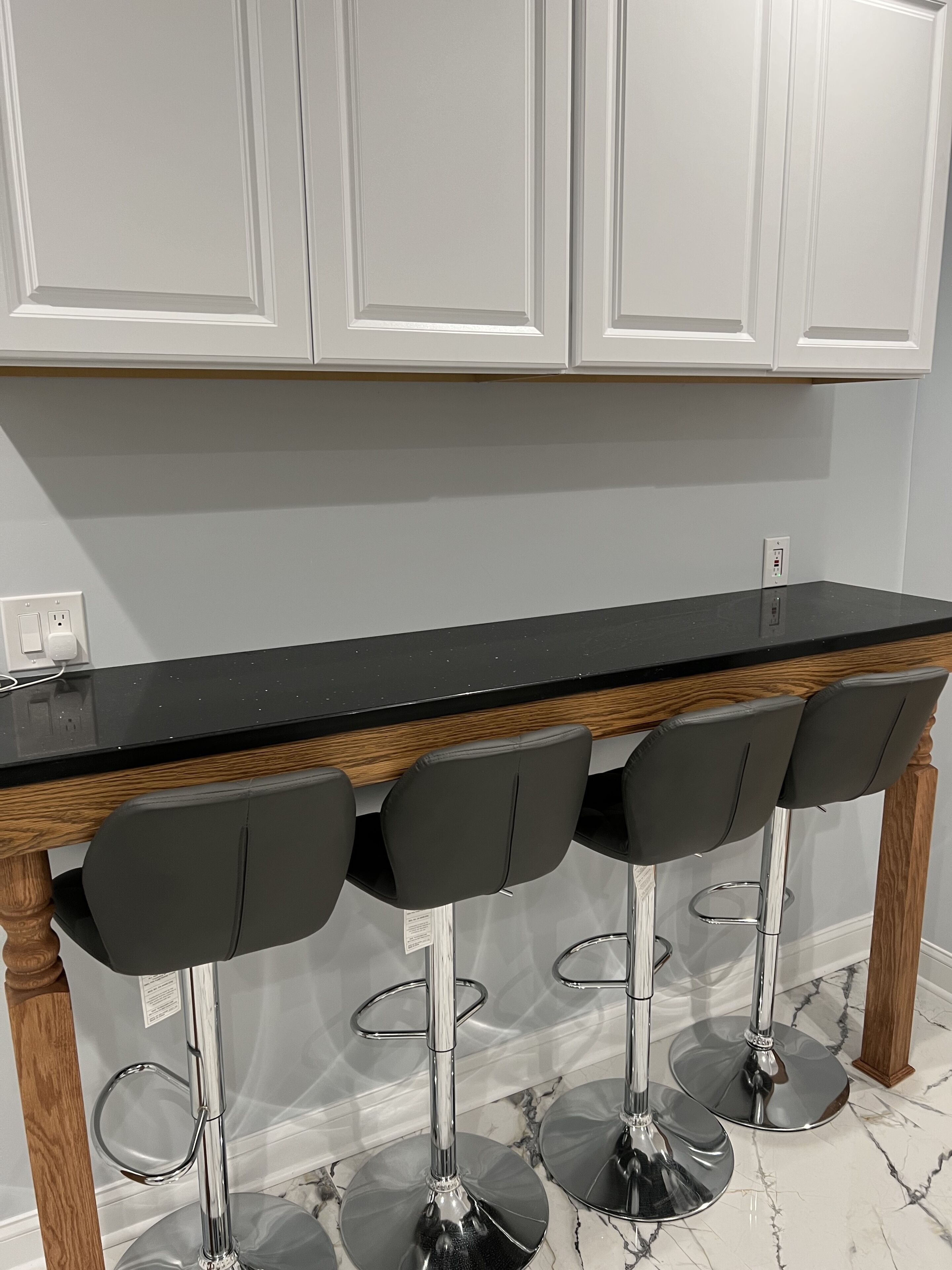 A kitchen with a black countertop, four bar stools, and white cabinets.