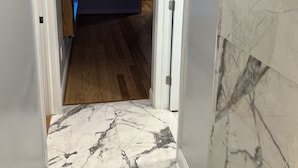 Un pasillo con suelo de mármol blanco, una habitación azul al fondo y una puerta que da a otra estancia.