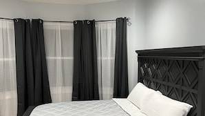 Un dormitorio moderno con cama, ventilador de techo y cortinas translúcidas.
