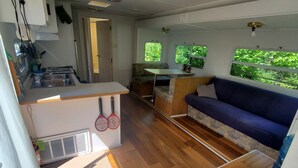 A compact RV interior with a kitchenette, a dining area, and a seating space with a view of greenery.