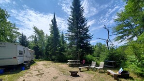 A campsite with a trailer, picnic tables, and chairs.