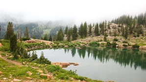 Um lago tranquilo rodeado por floresta densa e terreno rochoso.