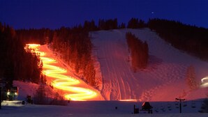 Pista de esqui coberta de neve à noite, com iluminação artificial criando um efeito espiral.