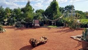 Een tuin met een hangmat, een houten sculptuur en een terras met een stoel en tafel.