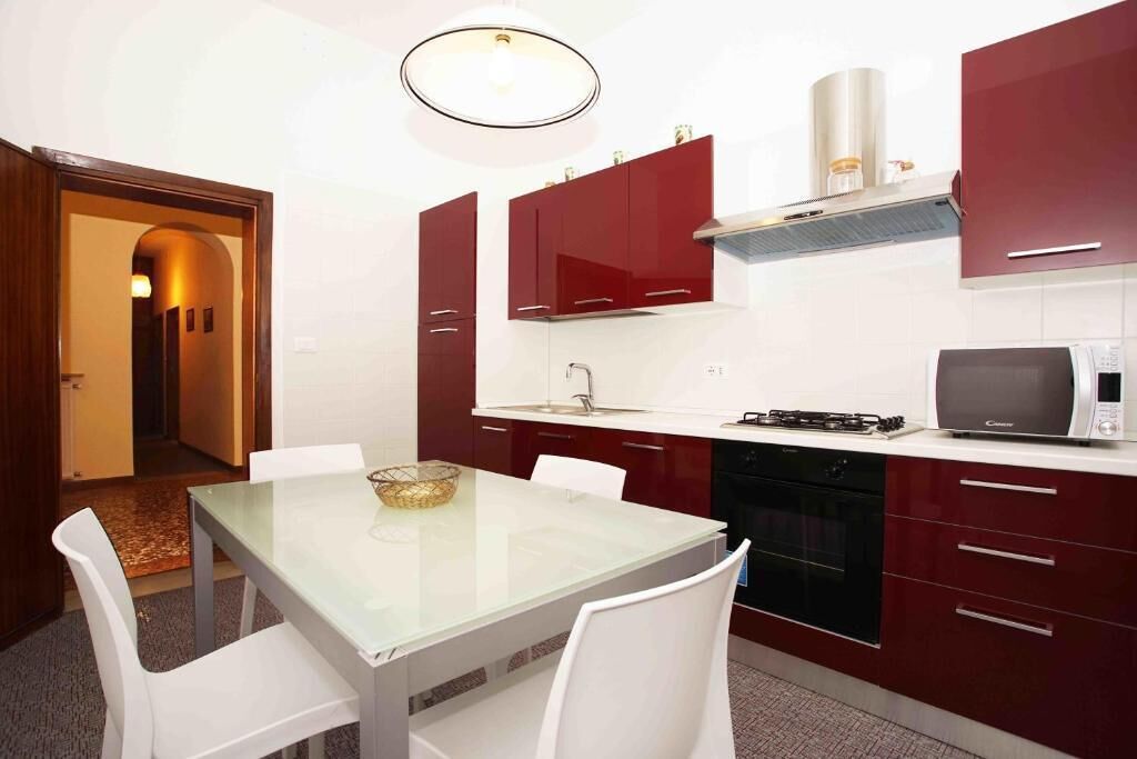 Une cuisine compacte avec une table à plateau en verre, des chaises blanches et des placards rouges.