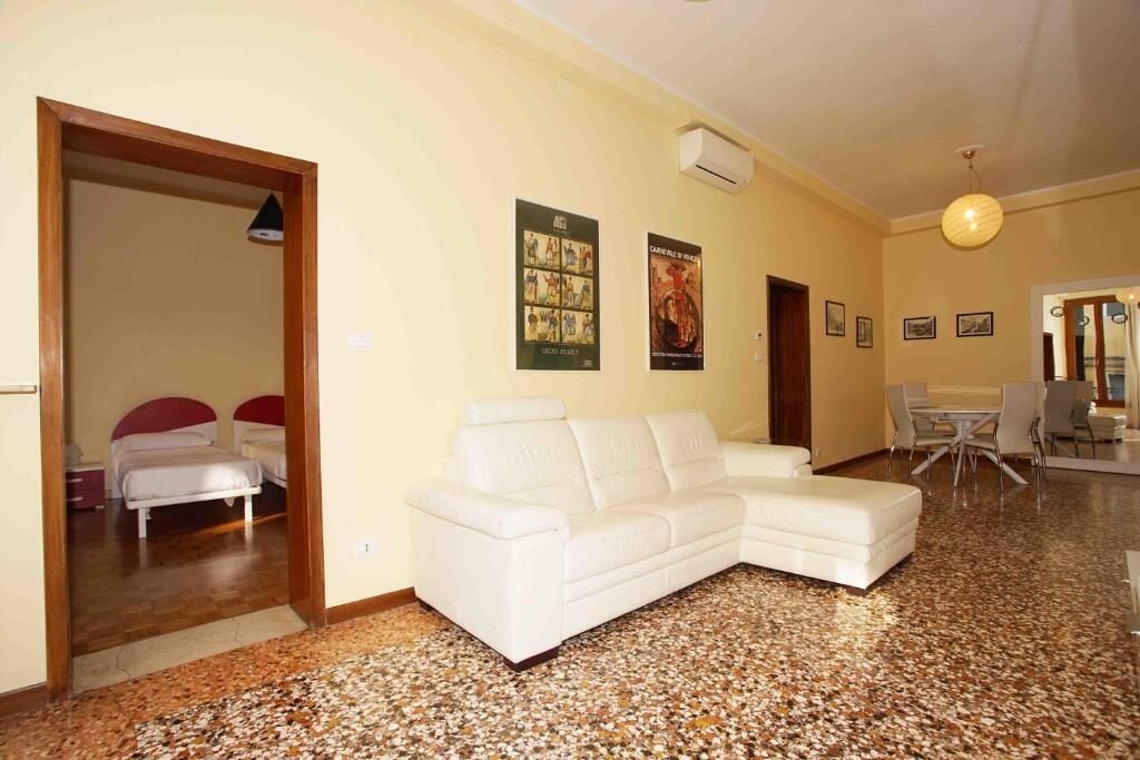 A modern living room with a white sofa, a dining area with a table and chairs, and a kitchen in the background.