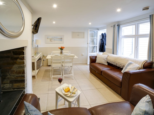 Un salon chaleureux avec une cheminée, un coin repas avec une table mise pour deux personnes et un canapé confortable.