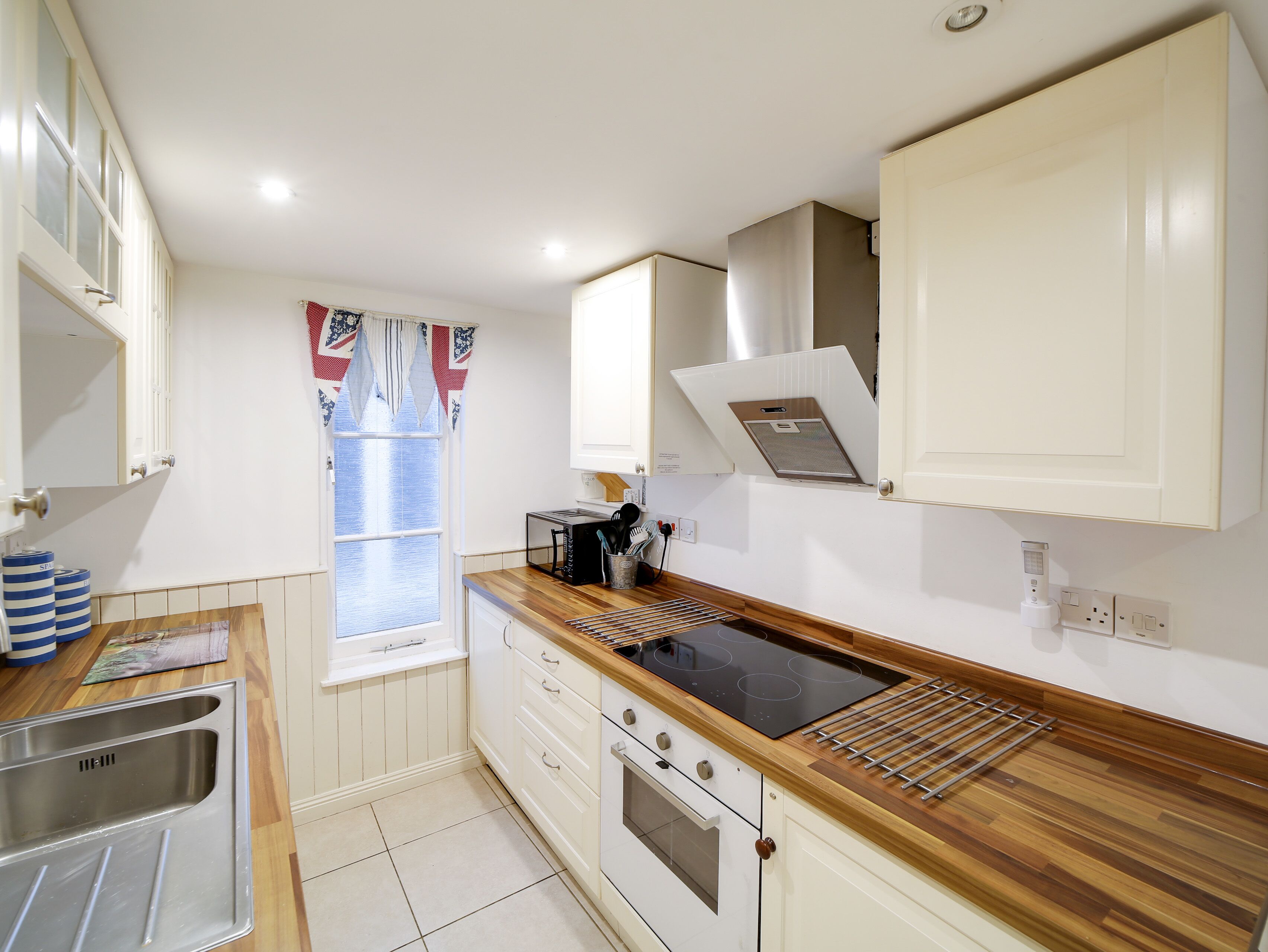 Cocina compacta con pileta, estufa y ventana con cortinas.