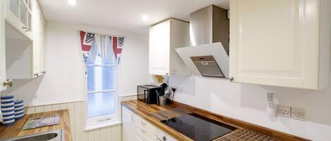 Cocina compacta con pileta, estufa y ventana con cortinas.