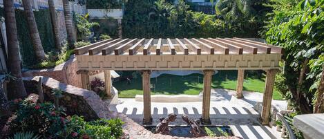 A covered outdoor area with a pergola, stone columns, and a central fountain.