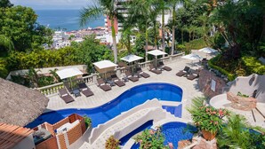 Zona de piscina en un resort con múltiples tumbonas, una piscina pequeña y una cascada.